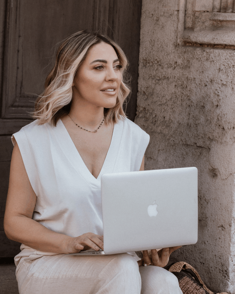 Ivana Andjić sedi sa laptopom u elegantnom ambijentu i simbolizuje pravu transformaciju kroz coaching program za žene